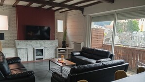 A living room with a fireplace, leather sofas, a coffee table, and a TV. - Lourdes: 5-Bedroom Duplex for 15 Guests, Central Location Near the Shrine (Lourdes)