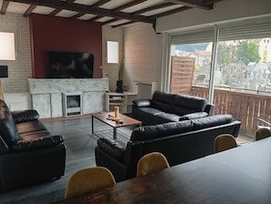 A living room with a fireplace, leather sofas, a coffee table, and a TV. - Lourdes: 5-Bedroom Duplex for 15 Guests, Central Location Near the Shrine (Lourdes)