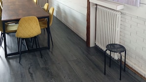 A dining area with a wooden table and yellow chairs, white brick walls, and a radiator. - Lourdes: 5-Bedroom Duplex for 15 Guests, Central Location Near the Shrine (Lourdes)