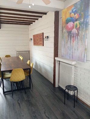 A dining area with a wooden table and yellow chairs, white brick walls, and a radiator. - Lourdes: 5-Bedroom Duplex for 15 Guests, Central Location Near the Shrine (Lourdes)