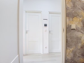 A hallway with two white doors, a small electronic device on the wall, and a textured wall on the right. - Cosy apartment for 4 guests with WIFI, TV and pets allowed (Dvůr Králové Nad Labem)