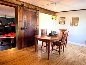 A dining area with a wooden table and chairs, a pool table, and a door with a rustic design. - Historic 5-bedroom house in Swanton perfect for family getaways (Swanton)