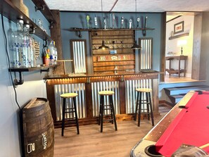 A bar area with stools, a wooden counter, and shelves with bottles and glasses. - Historic 5-bedroom house in Swanton perfect for family getaways (Swanton)