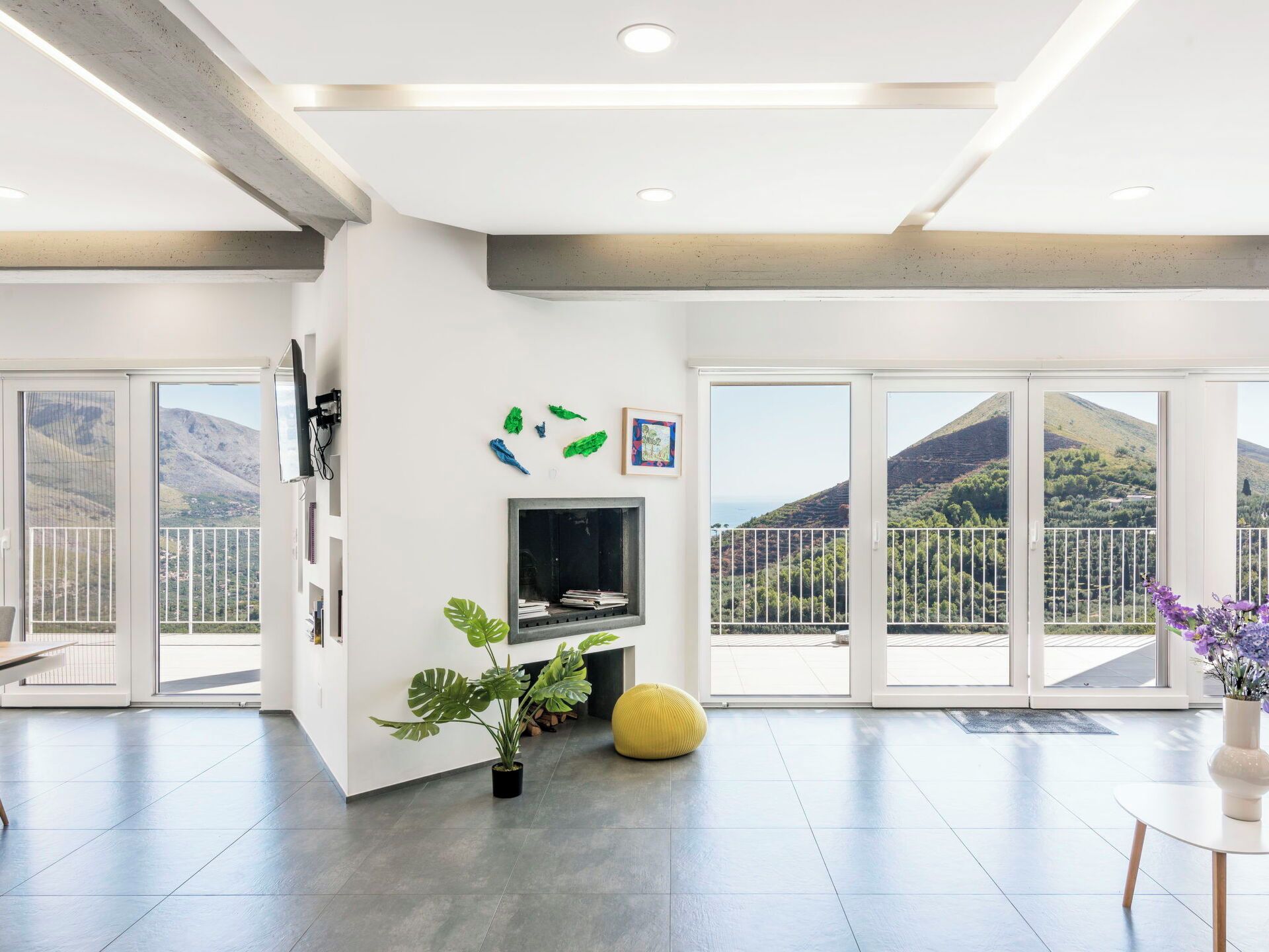 A spacious living area with a flat-screen TV, a potted plant, and a yellow ottoman.