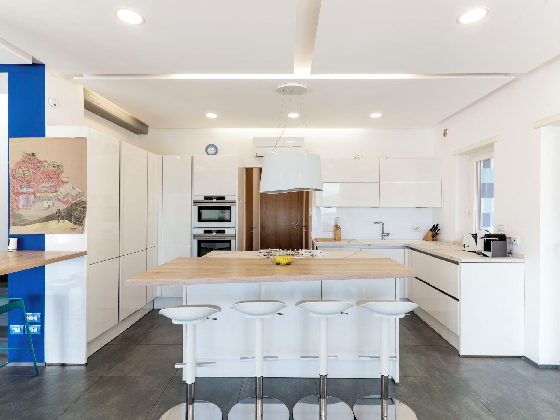 A modern kitchen with a central island, bar stools, and a hanging light fixture.