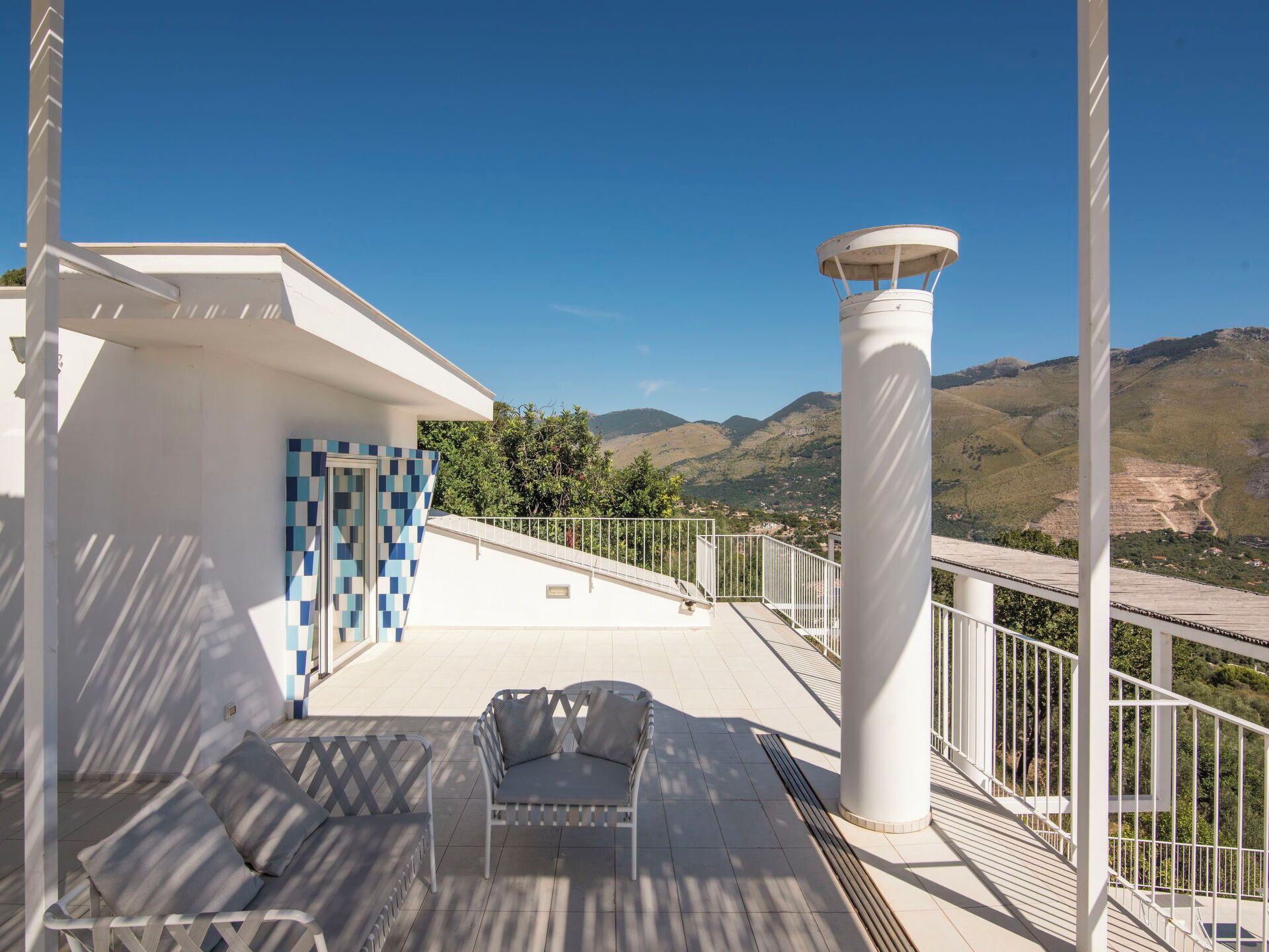 A balcony with a chair, a white column, and a view of the mountains.