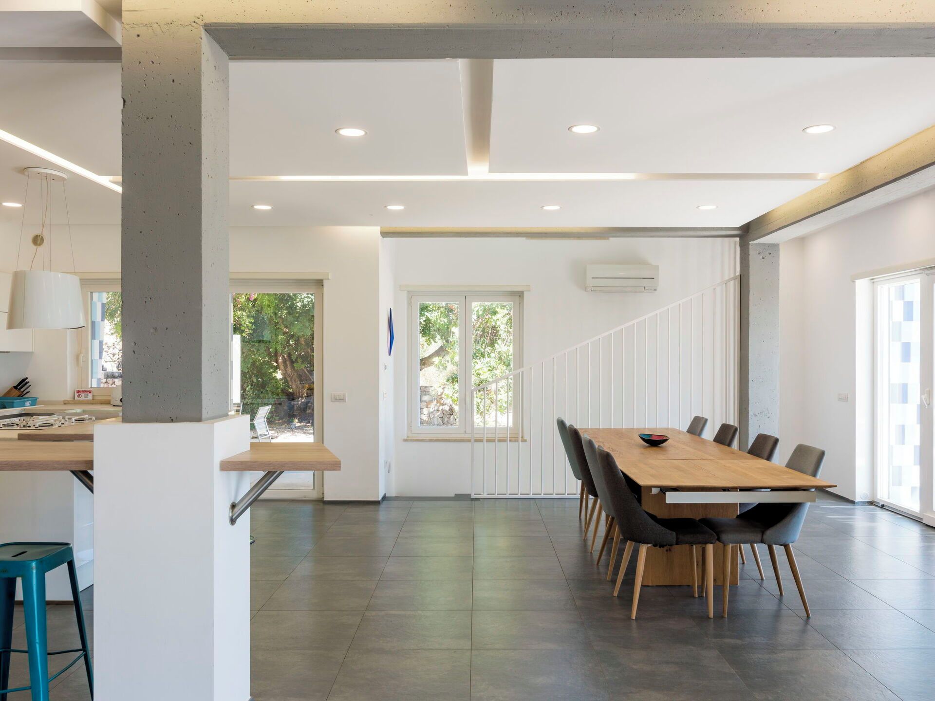 A modern interior with a long dining table, chairs, and a kitchen area with a countertop and stools.