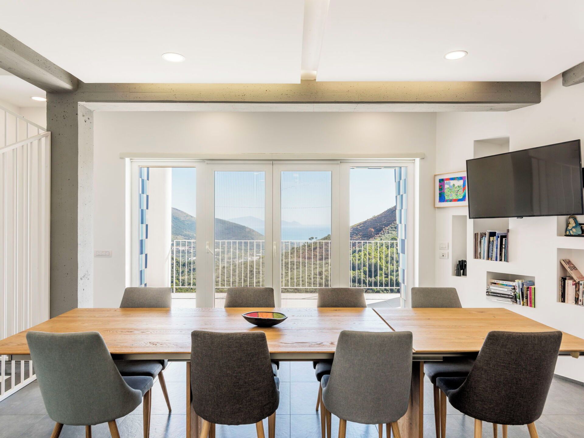 A modern dining area with a large table, six chairs, and a view of a mountainous landscape through large windows.