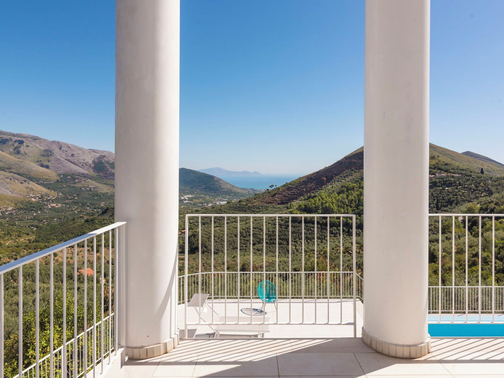 A balcony with a view of a mountainous landscape, white columns, and a blue railing.