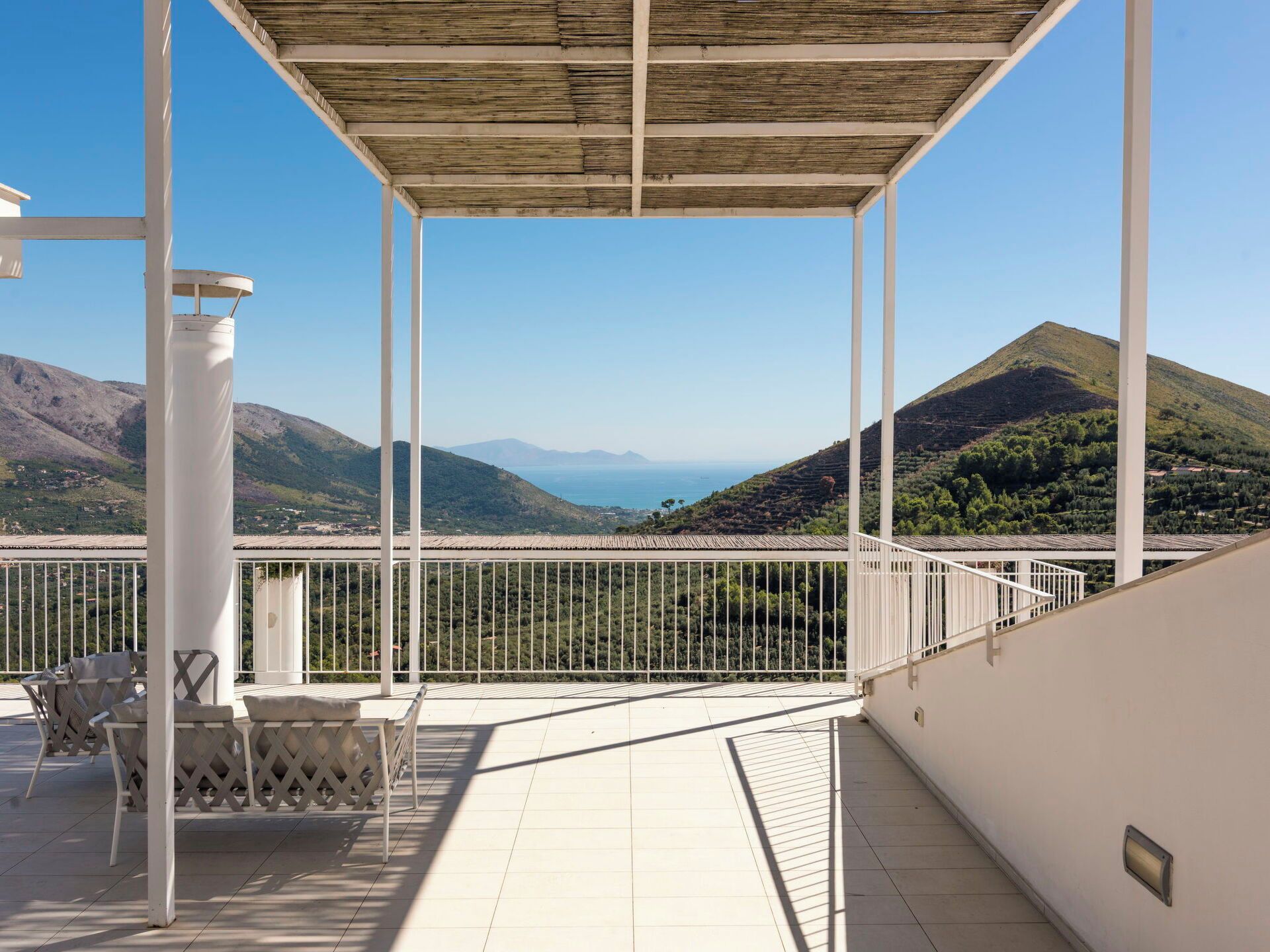 A covered outdoor terrace with a view of a mountainous landscape and the sea.