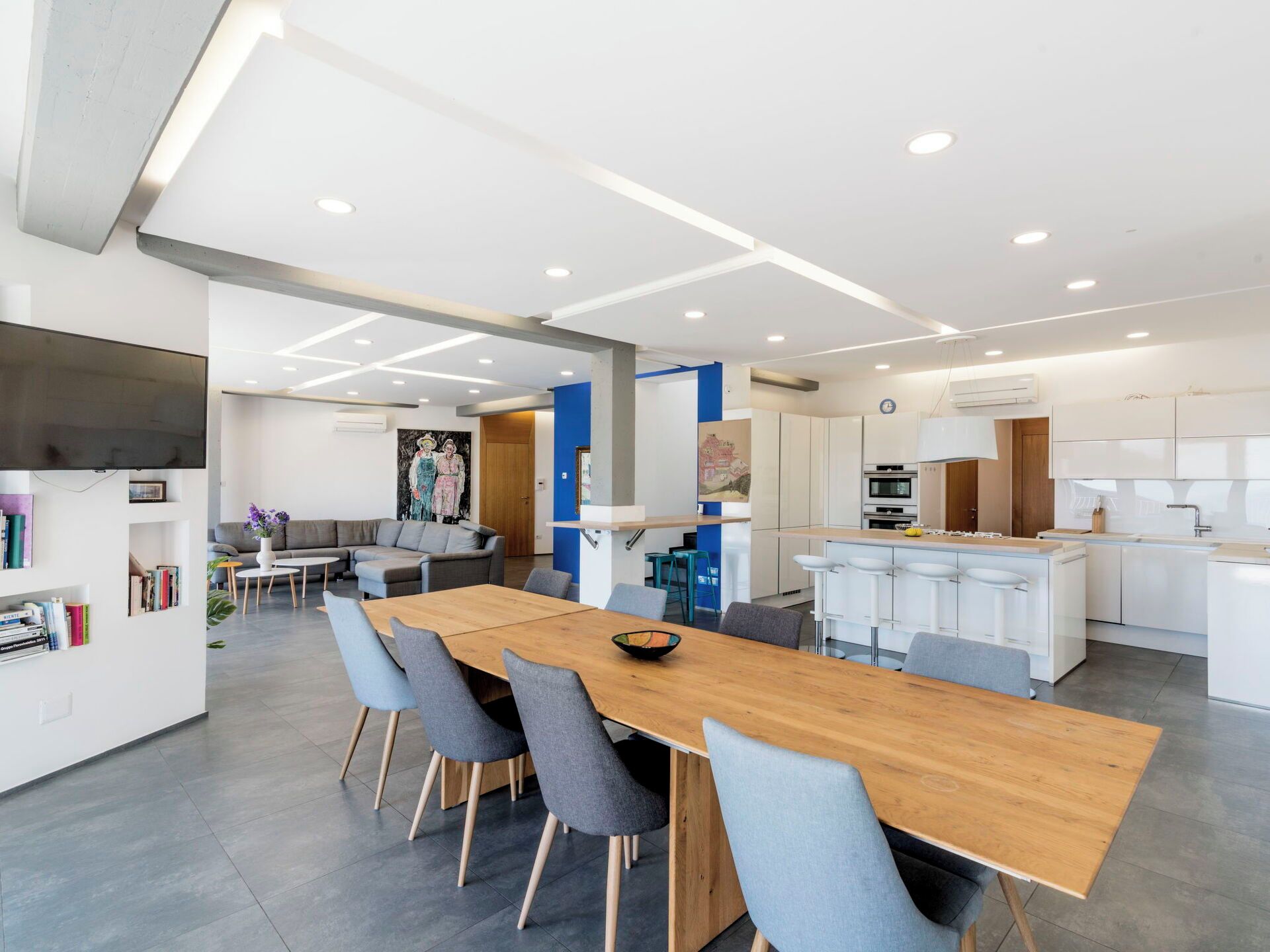 A modern kitchen with white cabinets, a built-in oven, and a dining area with a wooden table and grey chairs.
