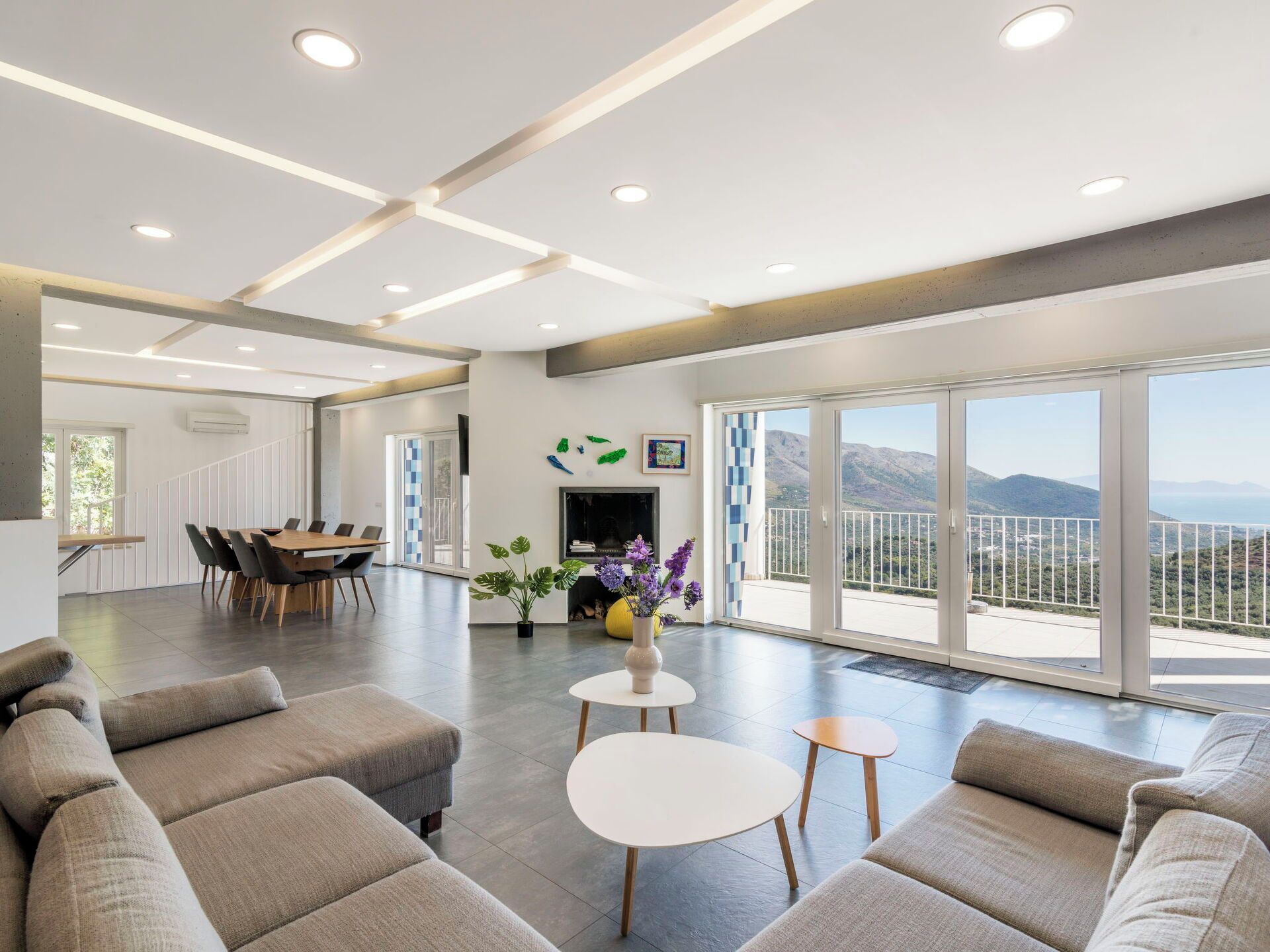 A spacious living area with a dining table, sofas, and a view of the mountains through large windows.