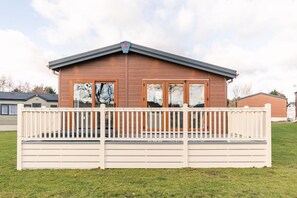 Ein zweistöckiges Holzhaus mit Flachdach, einem Balkon mit weißer Brüstung und großen Fenstern.
