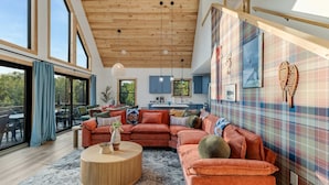 A spacious living room with a large sectional sofa, a round coffee table, and a view of the outdoors through large windows. - Close to Sunday River Hot Tub Sauna Cold Plunge (Bethel)