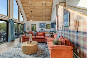 A spacious living room with a large sectional sofa, a round coffee table, and a view of the outdoors through large windows. - Close to Sunday River Hot Tub Sauna Cold Plunge (Bethel)