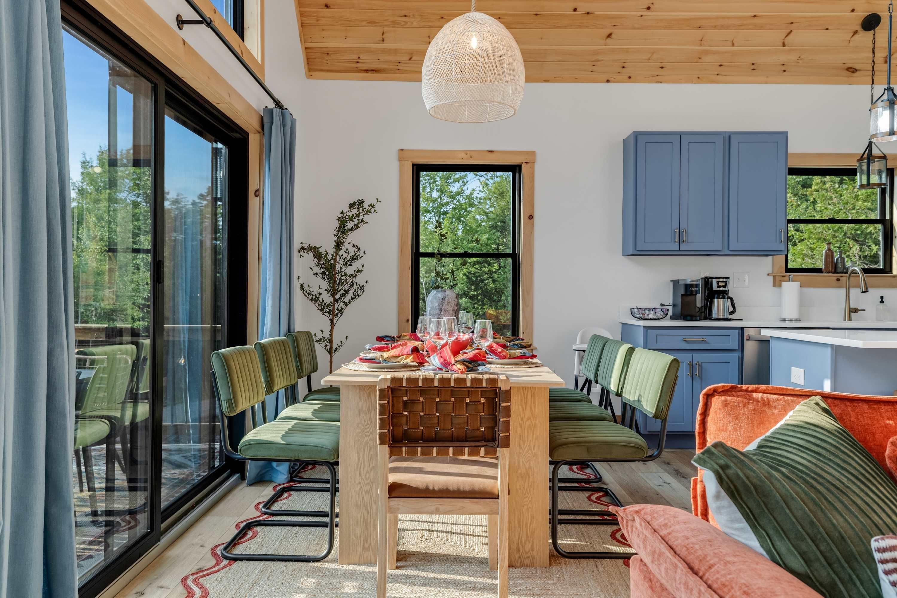 A modern kitchen with blue cabinets, a dining area with green chairs, and a large window.