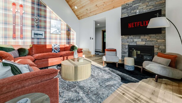 A modern living room with a fireplace, a large window with plaid curtains, and a Netflix sign. - Close to Sunday River Hot Tub Sauna Cold Plunge (Bethel)