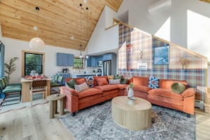 A modern living room with a wooden ceiling, a plaid-patterned wall, and a large sectional sofa. - Close to Sunday River Hot Tub Sauna Cold Plunge (Bethel)