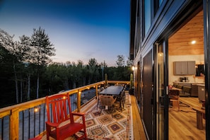 A deck with a table and chairs, a wooden bench, and a patterned rug. - Close to Sunday River Hot Tub Sauna Cold Plunge (Bethel)
