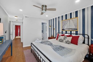 A bedroom with a bed, a bedside table, a nightstand, a ceiling fan, a wall-mounted painting, and a striped wall.