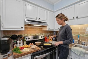 A kitchen with white cabinets, a stove, and a person cooking. - Beach Getaway w Pool Private Balcony (Atlantic Beach)