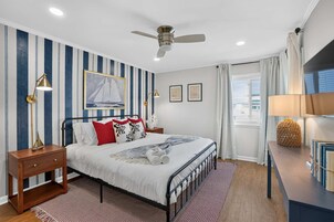 A bedroom with a bed, nightstands, a ceiling fan, striped wallpaper, and a window with curtains.