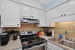 A kitchen with white cabinets, a stainless steel range, a coffee maker, and a sink. - Beach Getaway w Pool Private Balcony (Atlantic Beach)