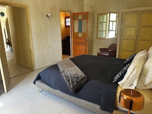 Ein Schlafzimmer mit einem Bett, einem Sessel, einem Kleiderschrank und einer Tür zu einem weiteren Raum.