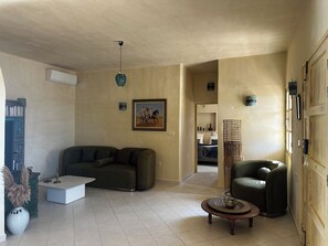 Una sala de estar con un sofá, una mesa de centro, una silla, un cuadro y una cesta de mimbre.