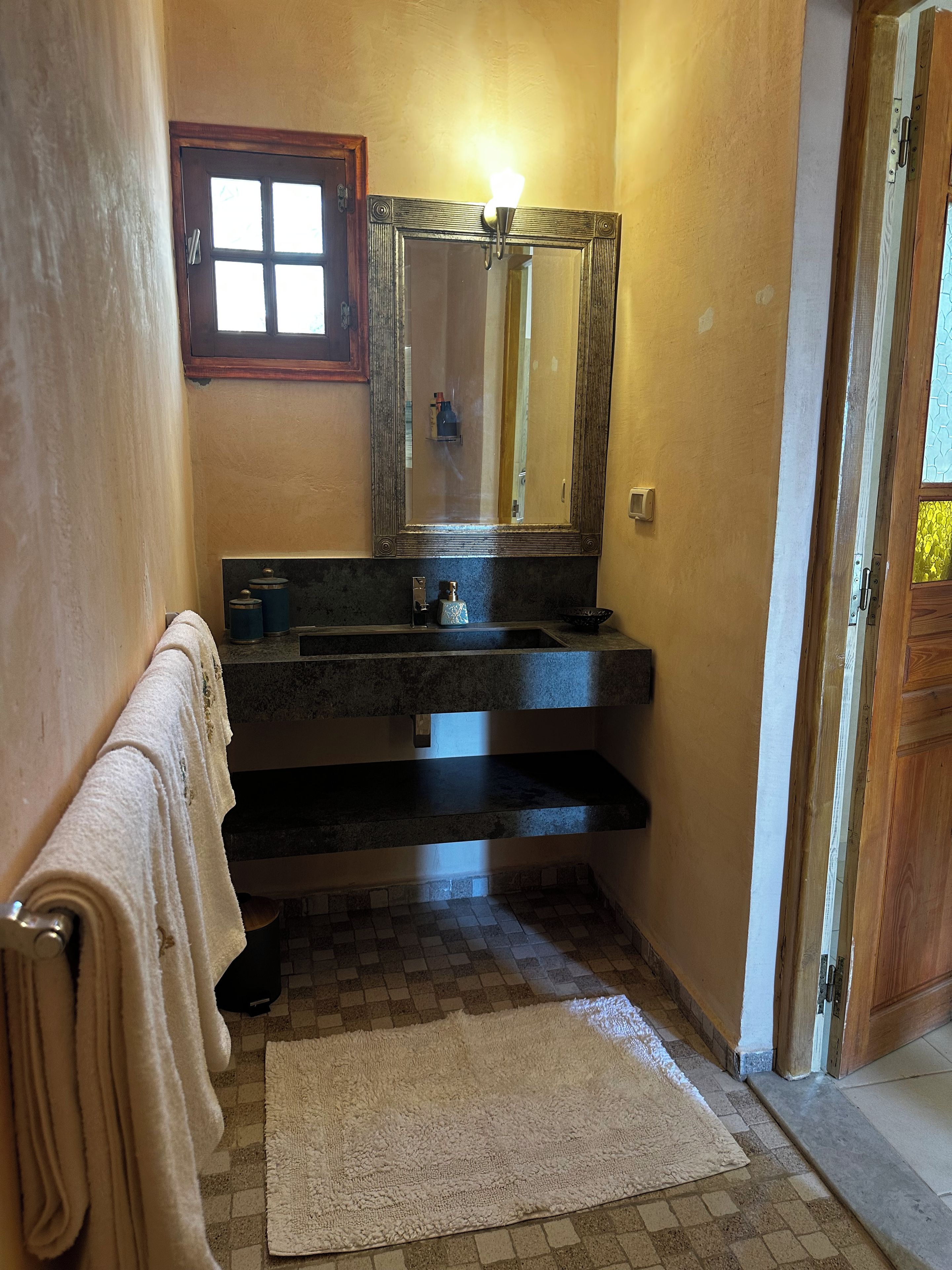 Un baño con un espejo grande, un lavamanos y un perchero para toallas.