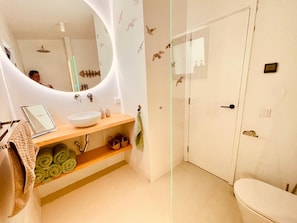 Et badeværelse med hvid vask, spejl, håndklædestang og toilet.