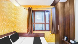 A hotel room with a bed, a wardrobe, a window with curtains, and a bedside table with a kettle and cups. - Townhouse Sindhi Camp (Jaipur)