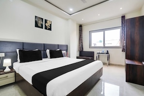 A hotel room with a large bed, bedside tables, a small table with a chair, a window with curtains, and artwork on the wall. - Townhouse Bhopal DB City Mall (Bhopal)