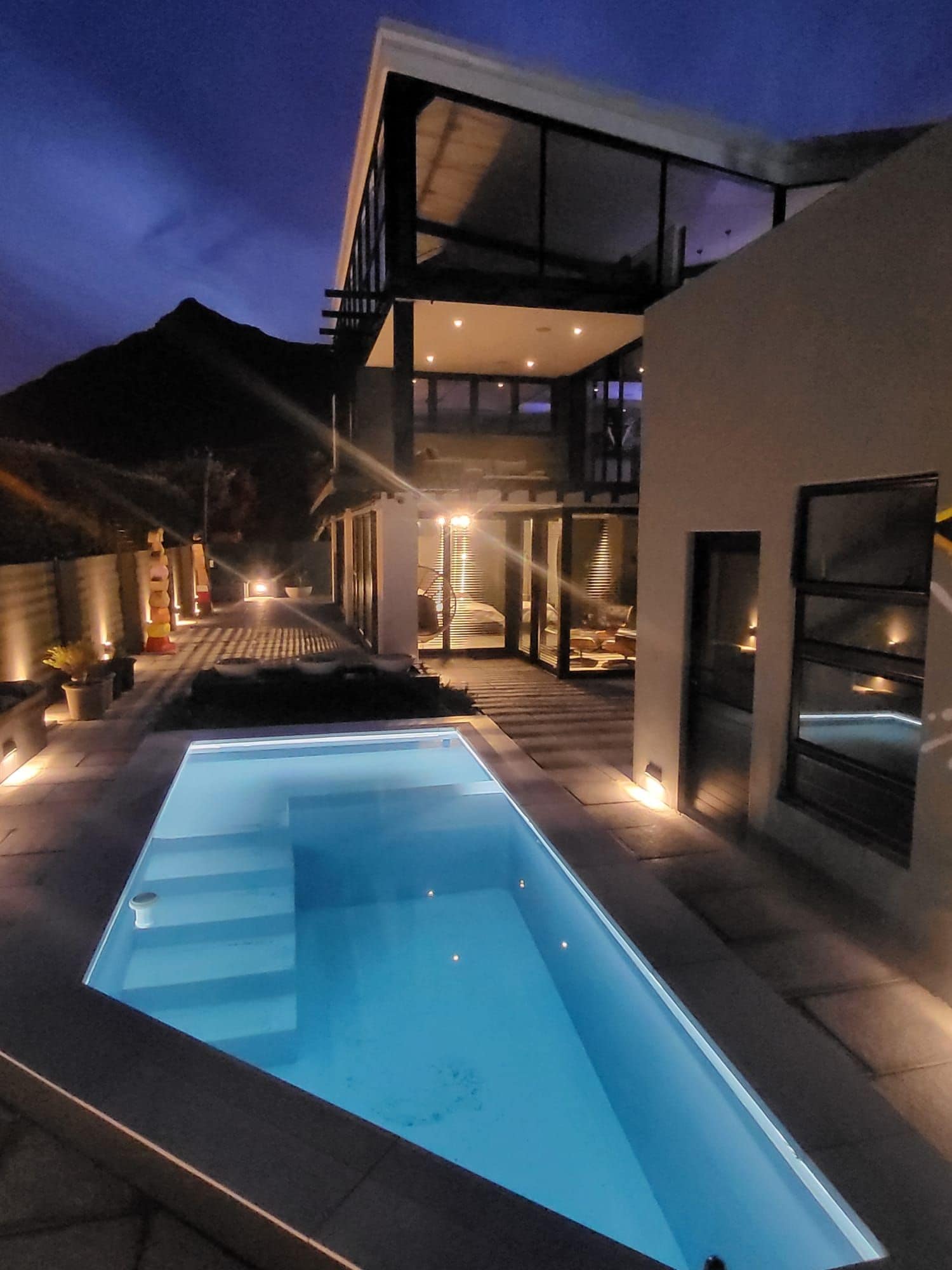 Ein modernes Haus mit Swimmingpool, Außenbeleuchtung und einem Berg im Hintergrund.