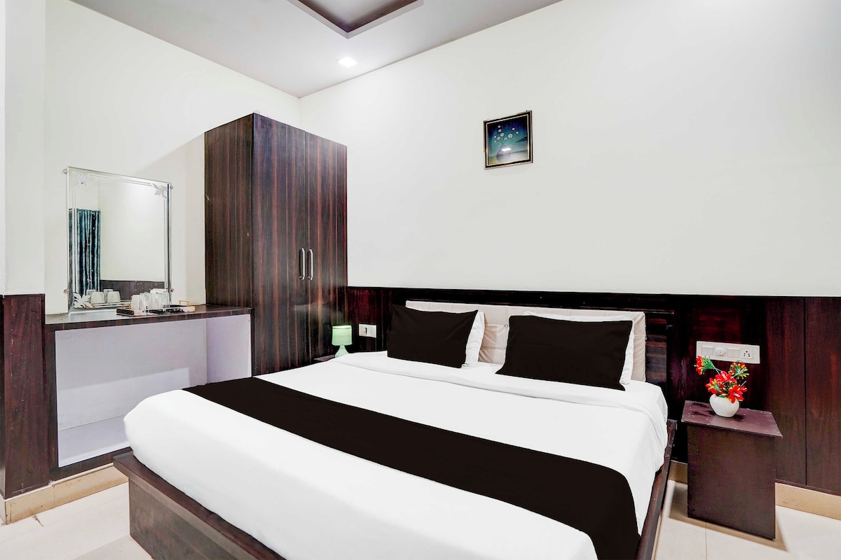 A hotel room with a large bed, a wardrobe, a bedside table with a lamp, and a small decorative item on the wall.