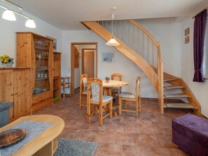 Un escalier en bois menant à un niveau supérieur, un coin repas avec une table ronde et des chaises, et un buffet en bois doté de portes en verre.