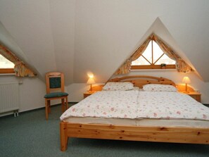 Ein Einzelbett mit Holzgestell in einem Zimmer mit schrägen Wänden und einem Vorhangfenster.