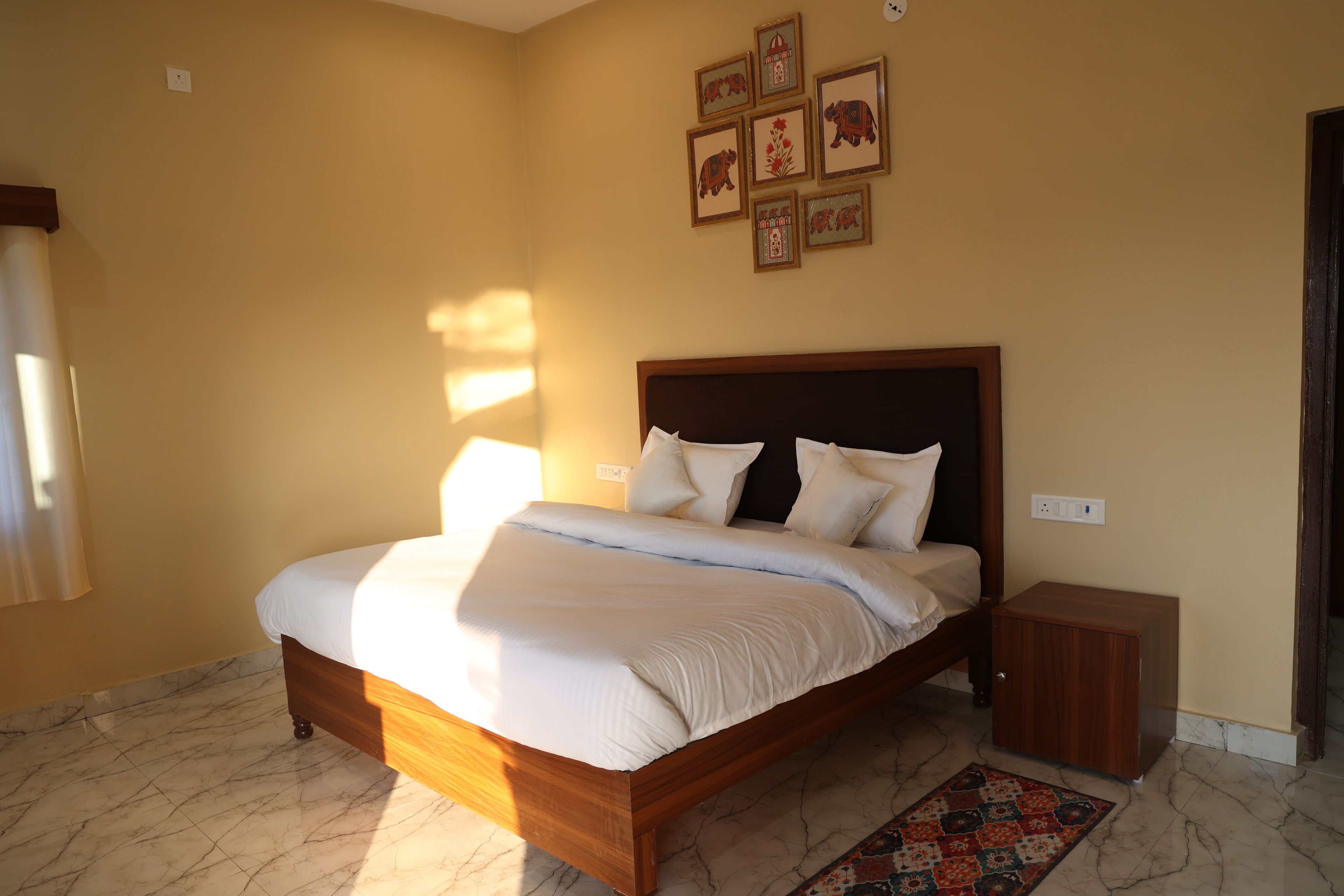 A bedroom with a bed, a nightstand, a wall-mounted power outlet, and a patterned rug.