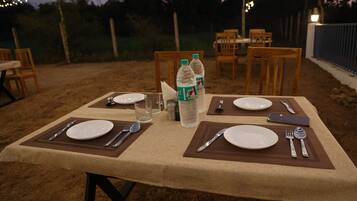 Un espacio de comedor al aire libre con mesas, sillas y guirnaldas luminosas.