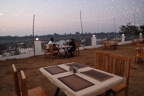 An outdoor dining area with tables and chairs, string lights overhead, and a view of a body of water. - Monkey River Resort  (Madla)