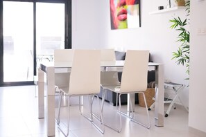 A modern dining area with a glass table and chairs, a sofa, and a plant on the wall. - Apartamento Naru (San Pedro del Pinatar) (San Pedro del Pinatar)