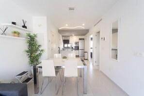 A modern kitchen with stainless steel appliances, a dining area with a white table and chairs, and a large potted plant. - Apartamento Naru (San Pedro del Pinatar) (San Pedro del Pinatar)