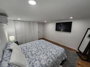 A bedroom with a bed, a TV on the wall, a wardrobe, and a bedside lamp.