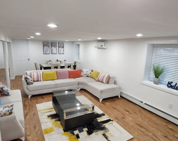 A modern living room with a sectional sofa, a glass coffee table, and a dining area with a table and chairs.