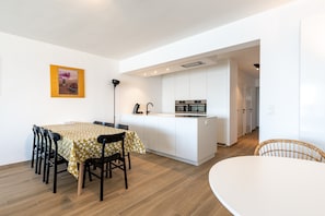 Eine moderne Küche mit weißen Schränken und Edelstahlgeräten, ein Essbereich mit Tisch und Stühlen sowie eine kleine Kücheninsel mit Spüle.
