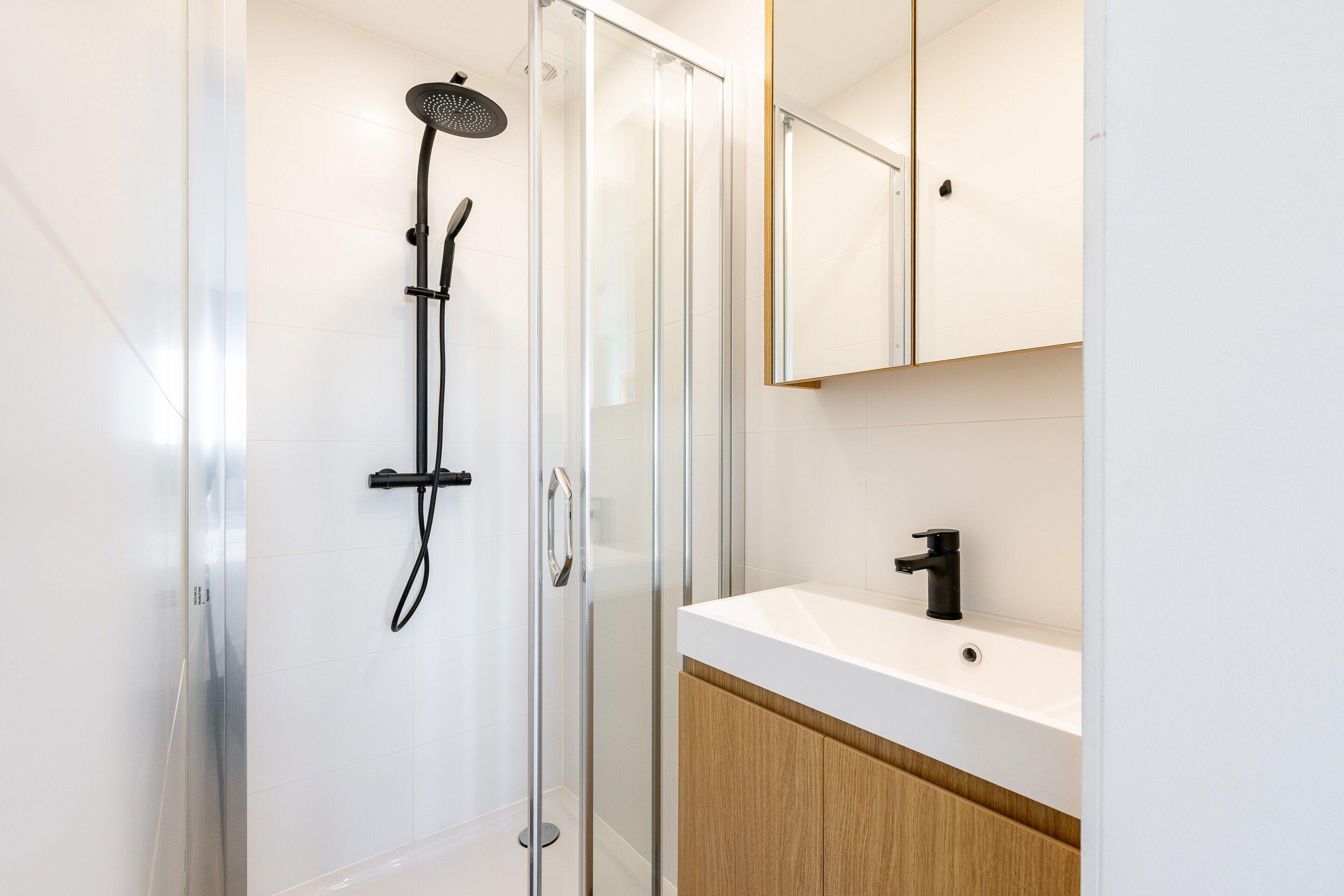 Un bagno moderno con doccia vetrata, lavandino bianco e mobiletto in legno.