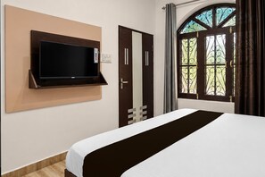 A hotel room with a bed, a mounted television, a door with a mirror, and a window with curtains. - Classic I APM Inn (Lucknow)