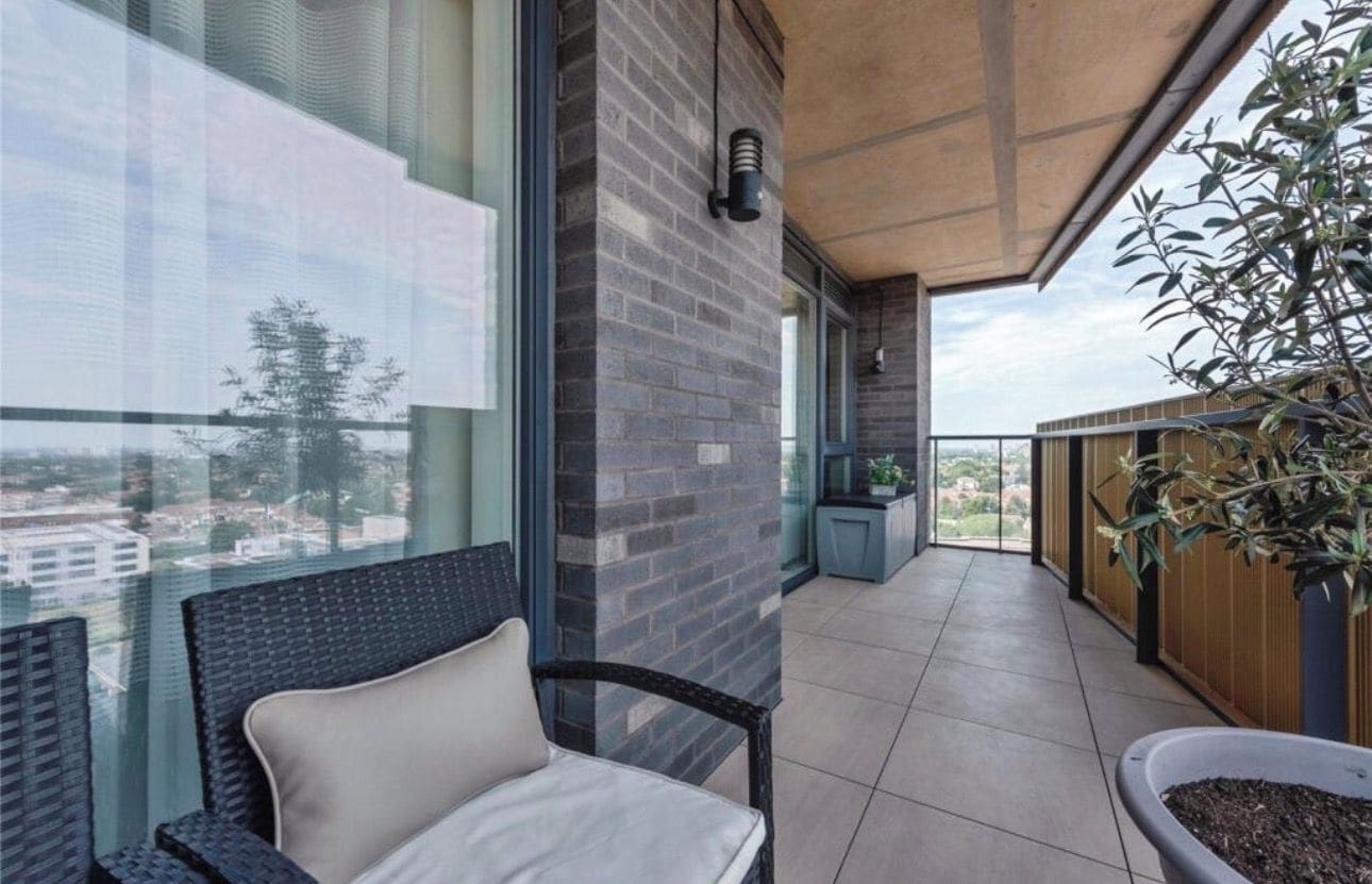 A balcony with a view of the city, a chair, a potted plant, and a small table.