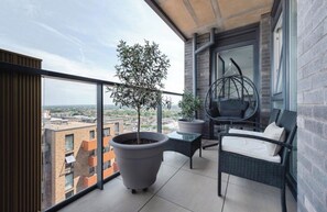A balcony with a potted tree, a hanging chair, and a wicker sofa. - Luxury Heathrow Apartment, 20min from London Central (Hounslow)