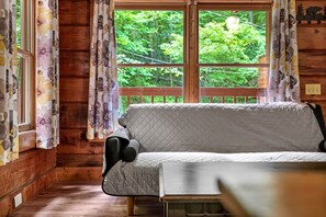 A wooden cabin interior with a sofa, curtains, and a view of greenery outside. - Charming Romantic Cabin Escape with Private Hot Tub in Sevierville, Tennessee (Sevierville)